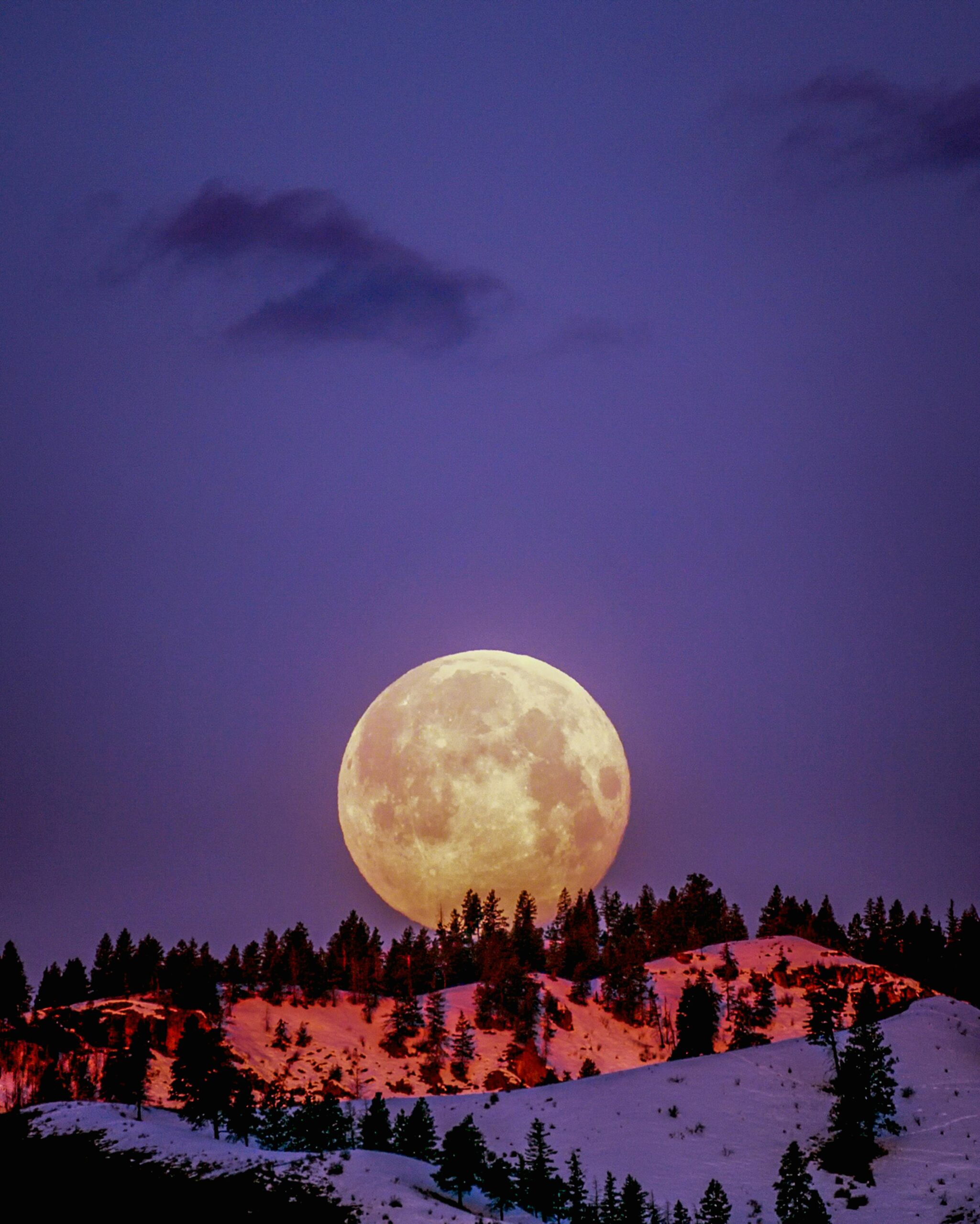 A breathtaking supermoon illuminating snow-covered hills under a purple sky in Wenatchee, WA.